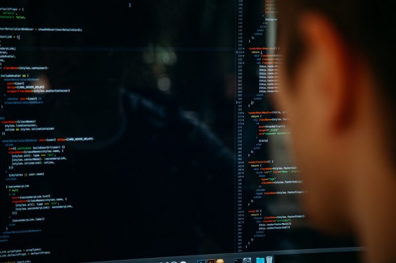 Na imagem aparece homem de costas, na frente de computador com códigos.