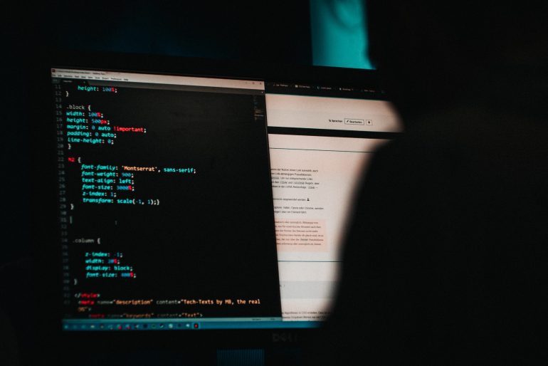 Sombra escura de uma pessoa na frente de um computador, na tela do computador aparecem códigos computacionais.
