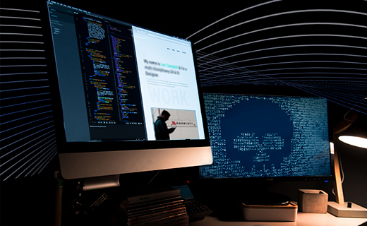Na imagem aparece duas telas de computadores, uma com o código do sistema, outra com uma caveira na tela.
