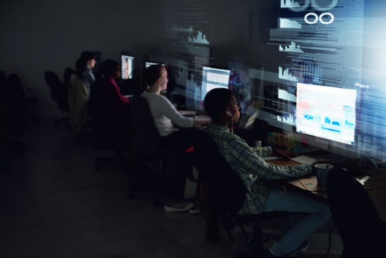 Na imagem aparece 4 pessoas em suas mesas de trabalho, visualizando dados e gráficos no computador.