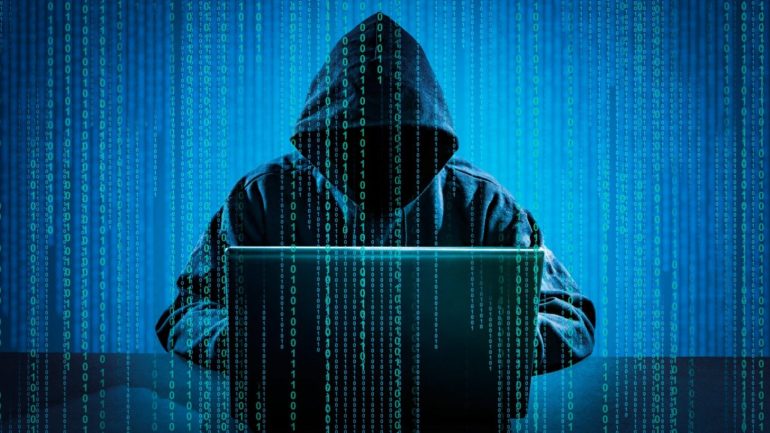 Imagem ilustrativa de um Hacker. Na imagem tem uma pessoa sentada no computador com um capuz na cabeça. Como sobreposição da imagem, códigos.