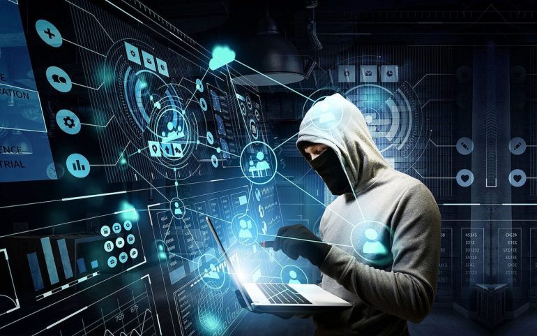 Na imagem aparece um hacker encapuzado com um computador em mãos acessando uma base de dados.